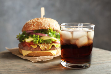 Glass of cold cola with tasty burger on table