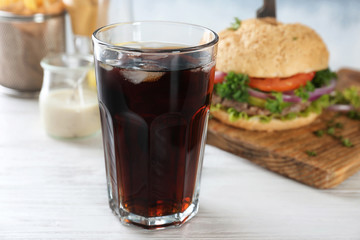 Glass of cold cola with tasty burger on table
