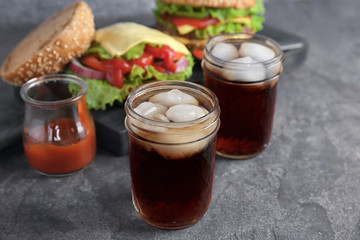 Jars of cold cola with tasty burgers on table