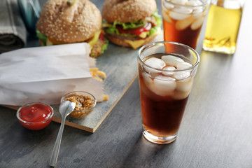 Glass of cold cola with tasty burgers on table