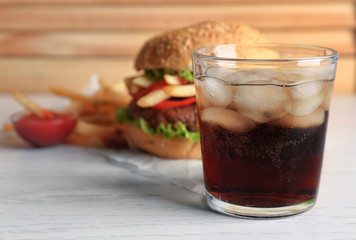 Glass of cold cola with tasty burger on table