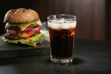 Glass of cold cola with tasty burger on dark background