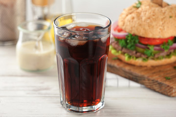 Glass of cold cola with tasty burger on table