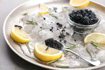 Obraz na płótnie Canvas Black caviar served with ice and lemon on metal plate