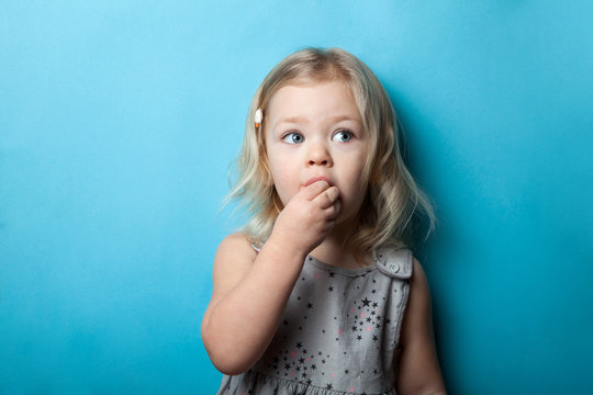 A little girl is isolated on a blue background eating a sweet candy.