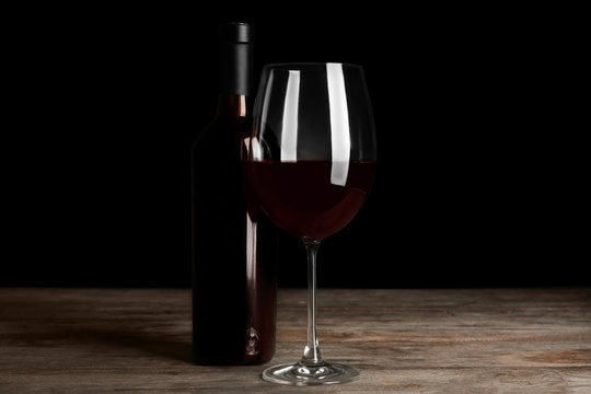 Bottle and glass with red wine on table against black background