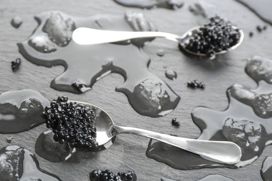 Spoons with black caviar on grey background
