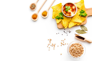 Middle Eastern cuisine. Bowl with hummus among pieces of crispbread and spices on white background top view copy space