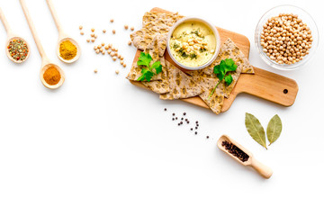 Middle Eastern cuisine. Bowl with hummus among pieces of crispbread and spices on white background top view copy space
