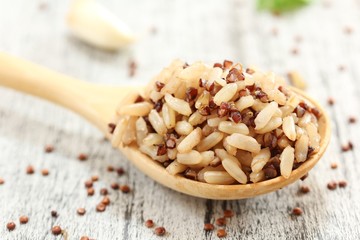 Cooked Quinoa brown rice in a wooden spoon on rustic white background, selective focus