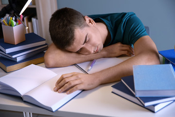 Tired student sleeping at his desk indoors. Preparing for exam