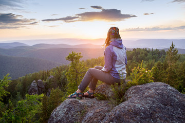 Naklejka na ściany i meble Young woman sitting on a rock, looking to the horizon