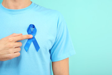 Man with blue ribbon on color background, closeup. Prostate cancer awareness