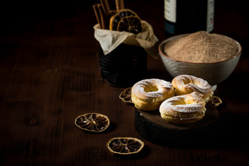 Three sweet cream puffs on dark board with cinnamon sugar in bowl and orange rings