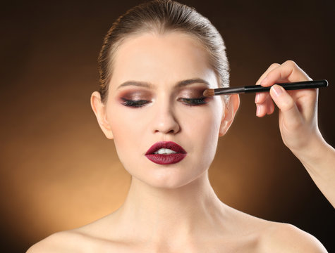 Professional visage artist applying makeup on woman's face on dark background