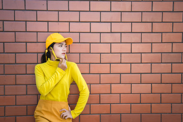 Portrait asian hipster girl on brick wall background,she wear yellow tone full body,Lifestyle of thailand people