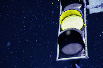 Snowy winter in the big city, flying snowflakes against yellow traffic light signal. Close up view.