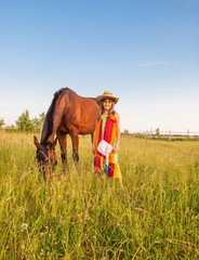 Little girl in cowboy hat with horse in meadow