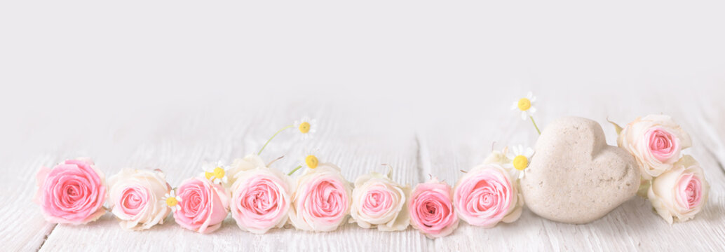 Pink roses and stone heart on rustic wooden background 