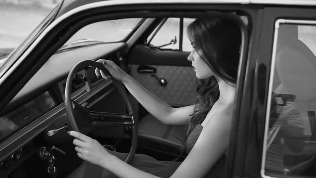 a young and beautiful woman who sits behind the wheel of a vehicle looks like a retro movie character, a lady sits in a chair and looks forward to the road