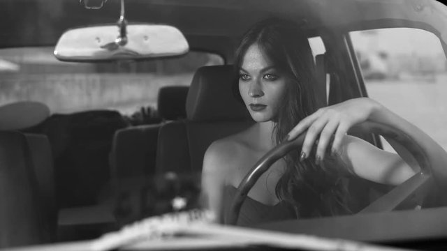 Amazing black and white shot of a beautiful model behind the wheel of nide retro car. She is mysteriously looking forward.