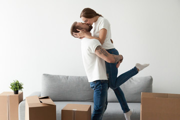 Happy loving couple kissing feeling excited about moving into new home, man lifting holding woman...