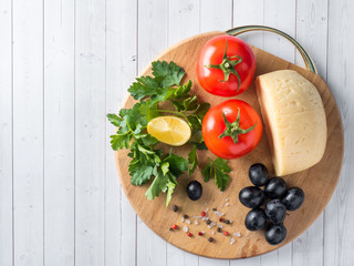 Piece of cheese with parsley, tomatoes grapes on a cutting Board.