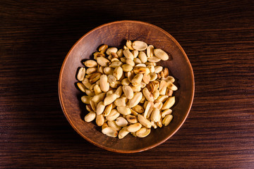 Peeled roasted peanuts in ceramic dish on wooden table. Top view