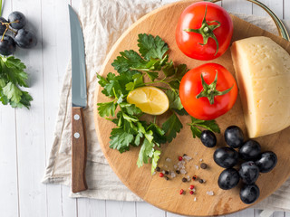 Piece of cheese with parsley, tomatoes grapes on a cutting Board with a knife