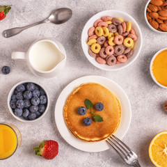 Breakfast with colorful cereal rings, pancakes, fruit, milk, juice.