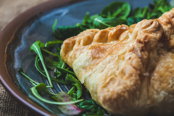 puff pastry stuffed with meat, carrots, potato pie, decorated with rucola, on a dark background. Background for postcard. Menu, restaurant, recipe concept, served in. Rustik stile