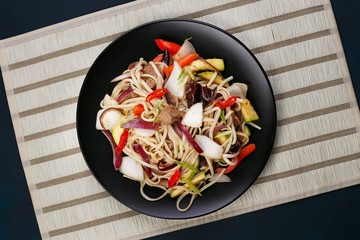 Udon wok noodles with pork and peppers, served on black plate, flat lay. Japanese cuisine