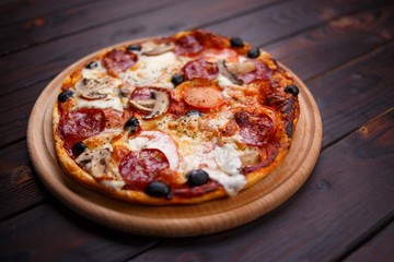 Freshly baked pepperoni pizza with mushrooms on the wooden plate, shallow depth of field