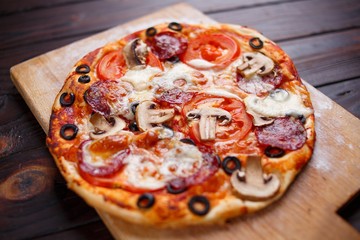Freshly baked pepperoni pizza with mushrooms on the wooden plate, selective focus, close up