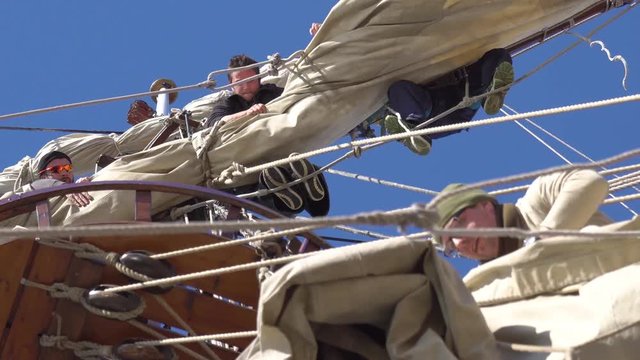 Sailors work with sails at a height on a traditional sailboat