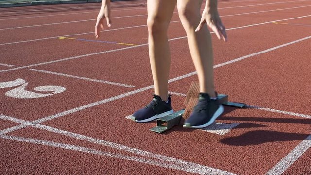 Professional blonde runner standing on starting blocks before race, slowmotion