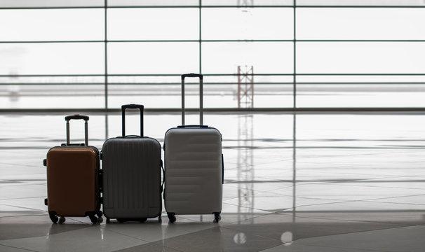 Travel concept. Suitcases on wheels are situating at airport building against glass wall. Empty hall interior with large windows. Copy space in the right side and focus on luggage
