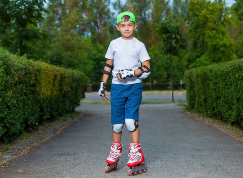 A little boy goes rollerblading in the summer in the park.