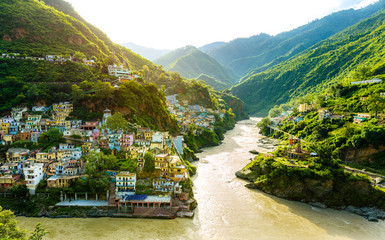 Confluence of two rivers Alaknanda and Bhagirathi give rise to the holy river of Ganga / Ganges at one of the five Prayags called Dev Prayag. Lush greenery in monsoons on the mountains. sunrise. India - obrazy, fototapety, plakaty