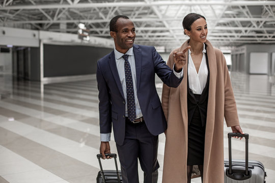 This is amazing. Delighted elegant business partners are going together with their suitcases. Man is pointing finger and expressing gladness while looking aside with smile. Copy space
