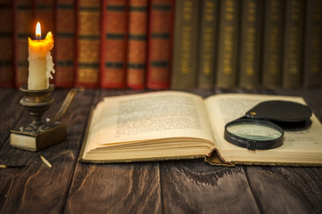 Obraz premium On the wooden background of the table there are stacks of colorful books near the old candlestick with burnt matches lying next to each other.