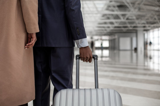 Travel concept. Close-up of arm of businessman is holding handle of suitcase while standing together with lady. Copy space in the right side. Back view