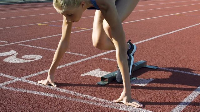 Beautiful female track runner leaves starting blocks in slow motion, competition