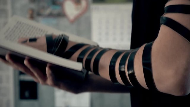 Hand of young jewish man with a tefillin on his arm, holding a psalms book, while reading a pray at a jewish ritual.