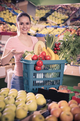 woman with basket with fresh greengrocery enjoying purchases in vegetable store