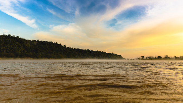 River Ganga / Ganges flowing in full force at Triveni Ghat, Rishikesh, Uttarakhand, India. Beautiful view around sunset/dusk/golden hour. Orange and blue skies with mountain in background