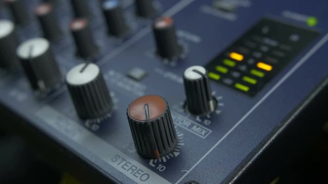 Close-up of female fingers turning fader knob on audio mixing desk. Lights of peak meter indicating volume levels on analog mixer console.
