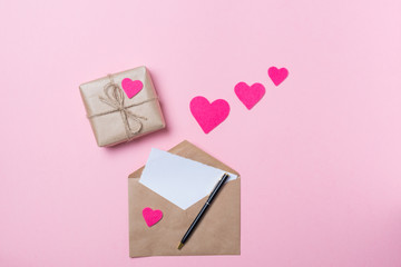 Craft envelope with blank paper, pen and gift with pink heart on pink background. Love concept. Saint Valentine's Day concept. Mother's day concept.