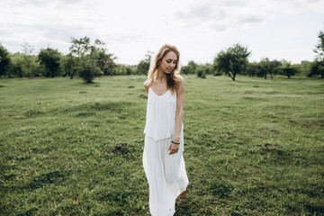 Young cute girl in white dress walking on green grass outdoors