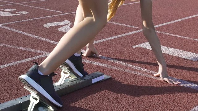 Experienced female runner leaving starting blocks, active workout in slow-mo